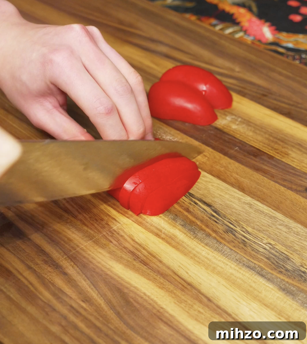 Red bell pepper being sliced on a wooden cutting board as prep for the chili oil shakshuka vegetable base.