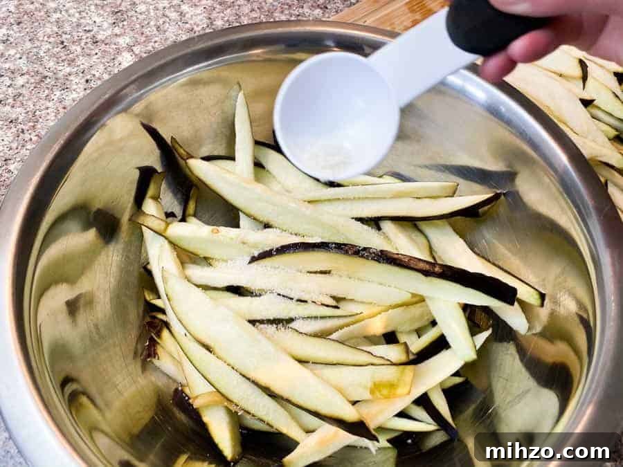 Eggplant slices in silver bowl, pouring salt in the bowl with white tsp