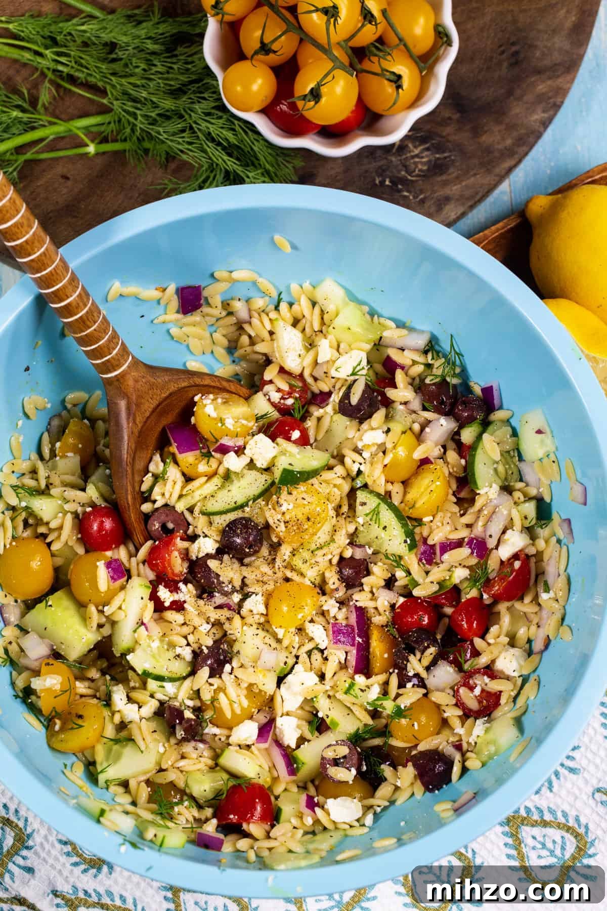 Greek Orzo in mixing bowl, fresh dill and bowl of cherry tomatoes.