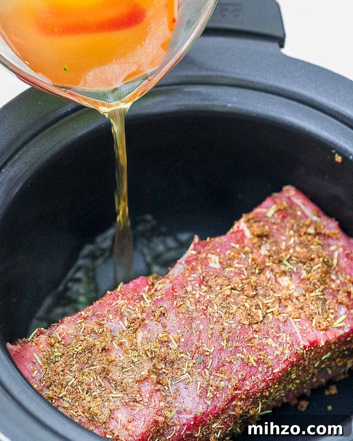 Pouring broth into slow cooker with tri tip inside.