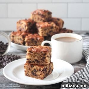 Stack of two cake squares on a white plate next to a cup of coffee.