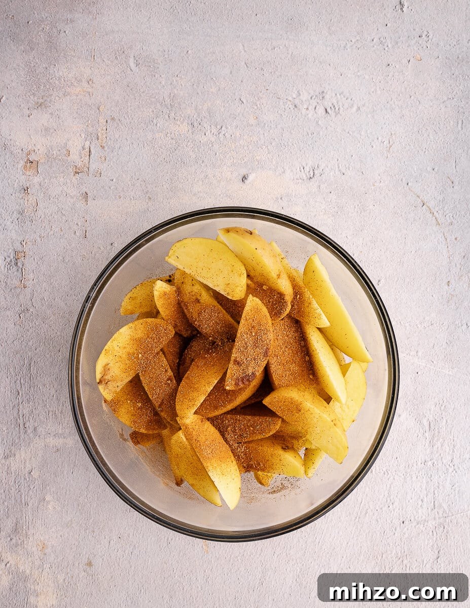 Crispy Oven-Baked Potato Wedges with Smoky Chipotle Sauce 12 a bowl of cut potatoes with taco seasoning on top.