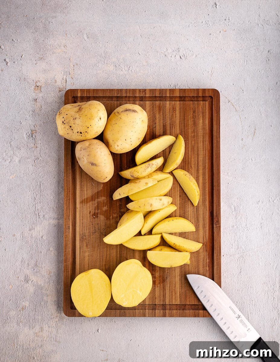 Crispy Oven-Baked Potato Wedges with Smoky Chipotle Sauce 5 gold potatoes cut into wedges on a cutting board.