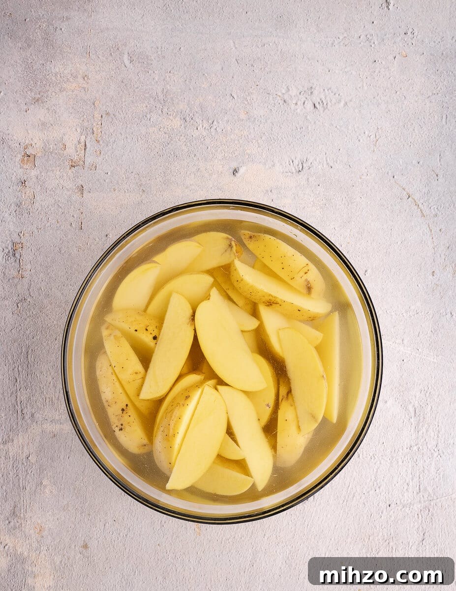 Crispy Oven-Baked Potato Wedges with Smoky Chipotle Sauce 7 gold potato wedges in a bowl covered with cold water.
