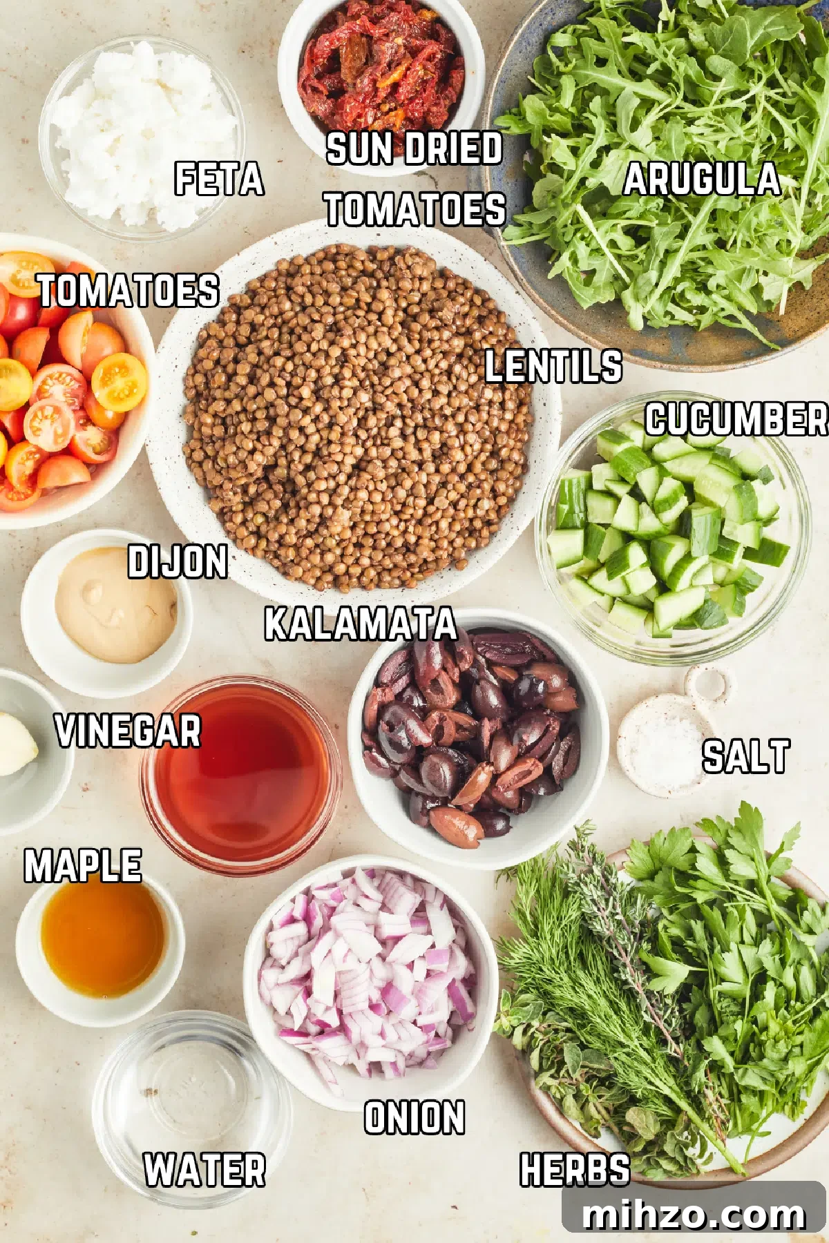 Salad with Lentils @spabettie #glutenfree #vegan #dairyfree #greeksalad #lentilsalad #dinner #recipe Overhead view of ingredient to make Mediterranean salad with lentils: crumbled feta, sun dried tomatoes, arugula, lentils, cucumber, tomatoes, Dijon, vinegar, kalamata olives, maple syrup, onion, fresh herbs, and water.