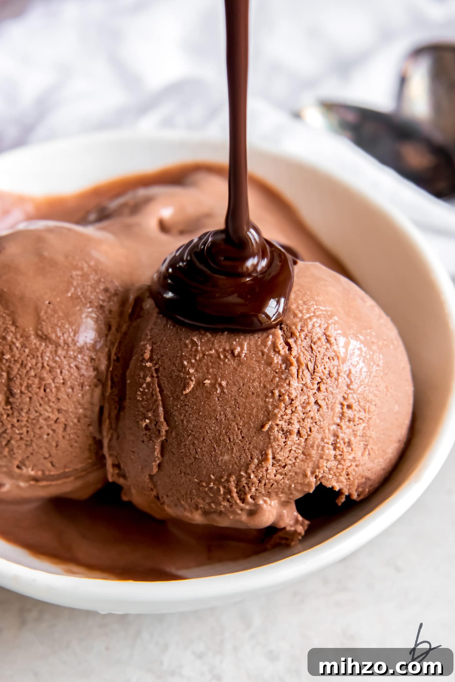 chocolate sauce being poured over scoop of no churn chocolate ice cream in a bowl