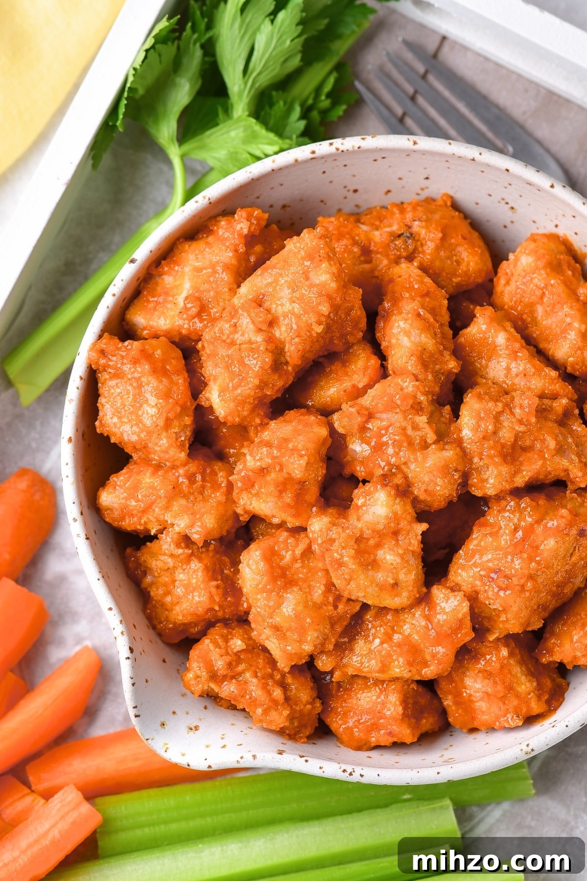 Air Fryer Buffalo Chicken Bites (Gluten-Free, Dairy-Free) A bowl of air fryer buffalo chicken bites with veggies on tray.