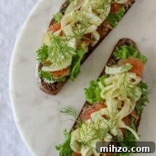 Open sandwiches topped with lettuce, salmon and fennel on a marble plate