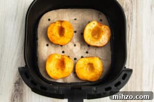 Crispy Air Fryer Peaches with Honey-Brown Sugar Glaze 11 Picture of air fryer with parchment paper liner and peaches halves on top.