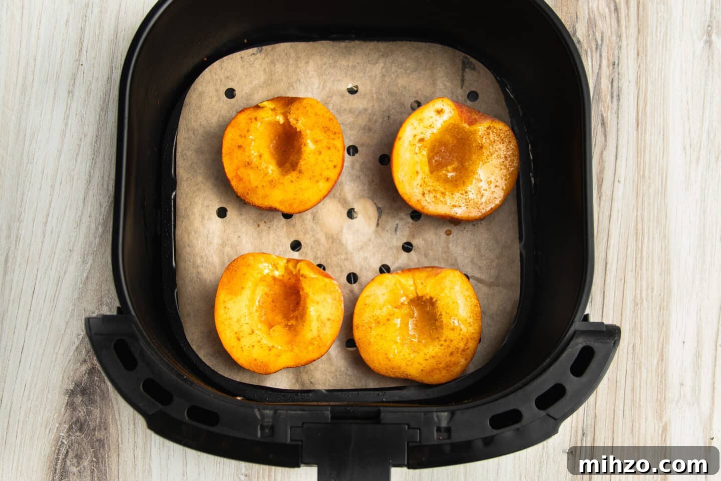 Crispy Air Fryer Peaches with Honey-Brown Sugar Glaze 6 Picture of air fryer with parchment paper liner and peaches halves on top.