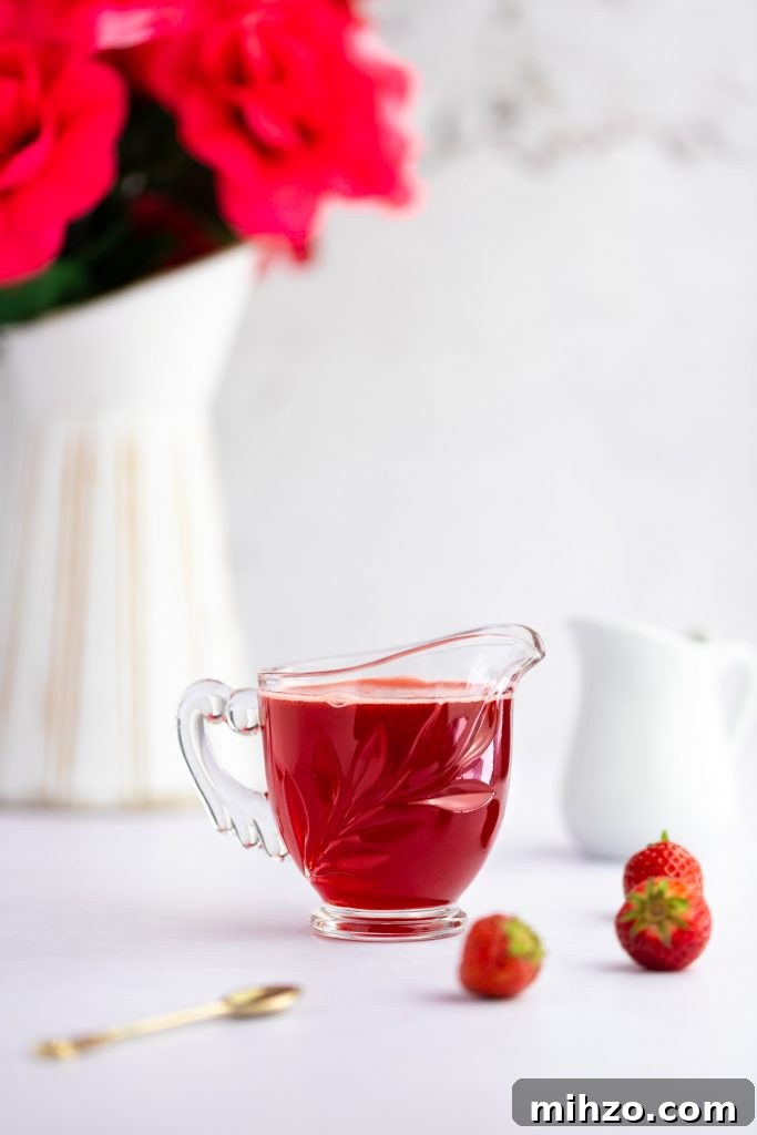 Strawberry Simple Syrup Recipe for Drinks and Desserts 2 Container of simple syrup, next to three strawberries, a small spoon and a white vase with pink roses in the background.