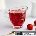Close up photo of strawberry simple syrup, next to strawberries and a gold spoon.