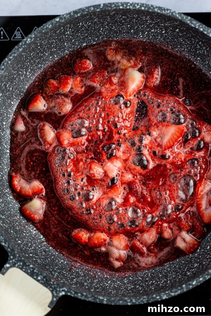 Strawberry Simple Syrup Recipe for Drinks and Desserts 4 Overhead photo of strawberry syrup with chunks of strawberries simmering in a pan.