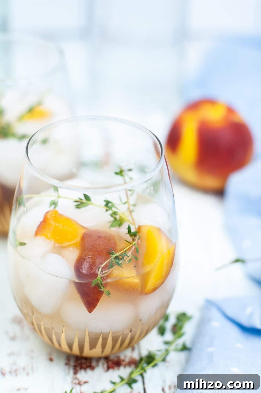 Peach gin cocktail in a glass dressed with peach wedges and thyme sprigs