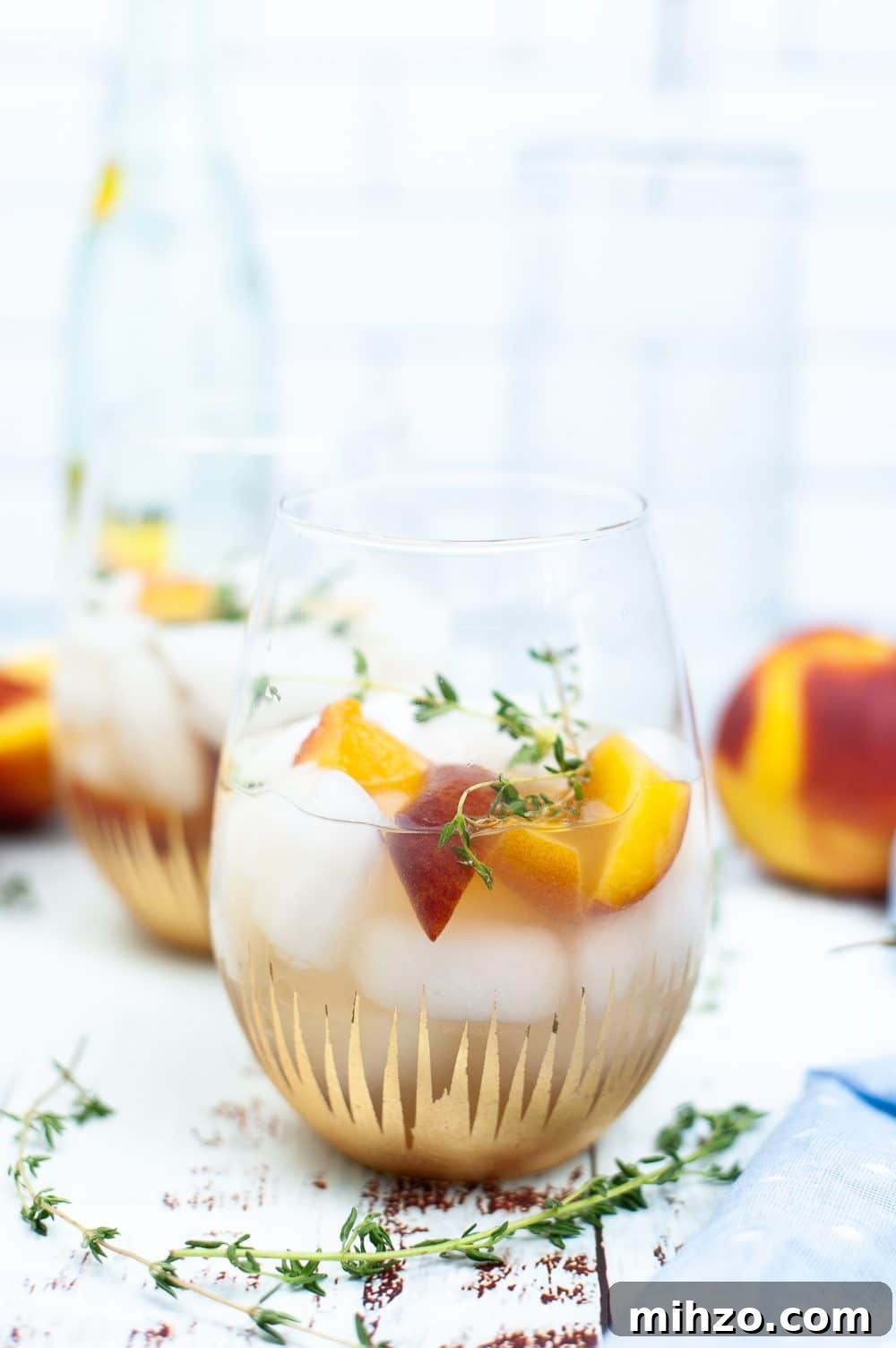 Peach syrup cocktail in a glass dressed with slices of peaches and thyme sprigs
