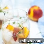 Peach gin cocktail in a glass dressed with peach wedges and thyme sprigs