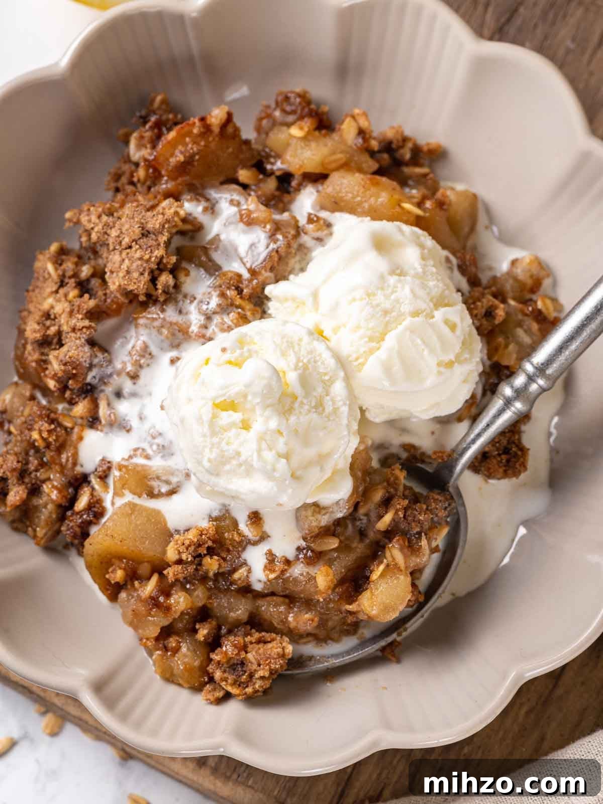 apple crisp in bowl with ice cream and pewter spoon.
