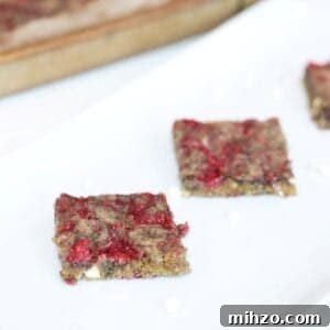 Raspberry White Chocolate Blondies with Raspberry Swirl 9 Two Raspberry and White Chocolate Blondies on a white platter with a bar pan of blondies in the background.