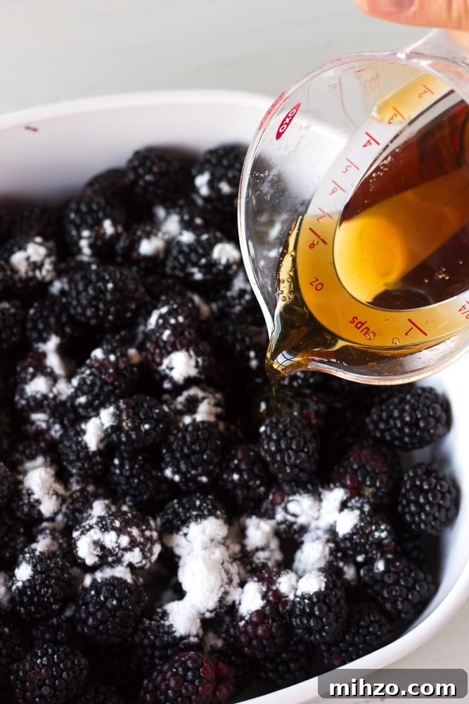 maple syrup being poured over blackberries in a baking dish.