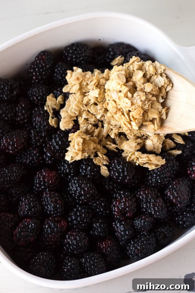 Spooning oat topping over blueberries in a baking dish.