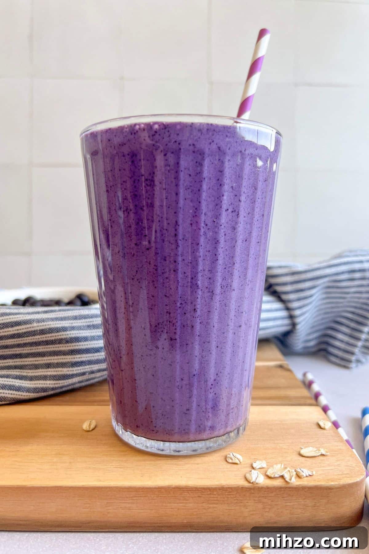 Thick, refreshing, and packed with 35 grams of protein, this blueberry smoothie makes the easiest healthy breakfast to take on the go. Blueberry protein smoothie in a glass with a straw on a cutting board.