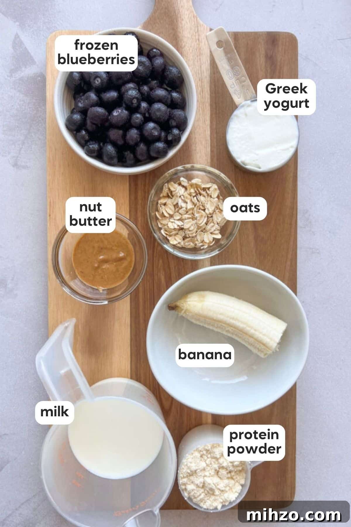 Thick, refreshing, and packed with 35 grams of protein, this blueberry smoothie makes the easiest healthy breakfast to take on the go. Labeled photo of ingredients in blueberry protein shake displayed on a wooden board on a marble counter