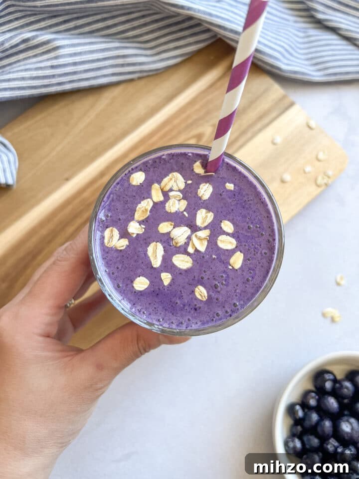 Thick, refreshing, and packed with 35 grams of protein, this blueberry smoothie makes the easiest healthy breakfast to take on the go. blueberry muffin smoothie in a glass with a purple striped straw