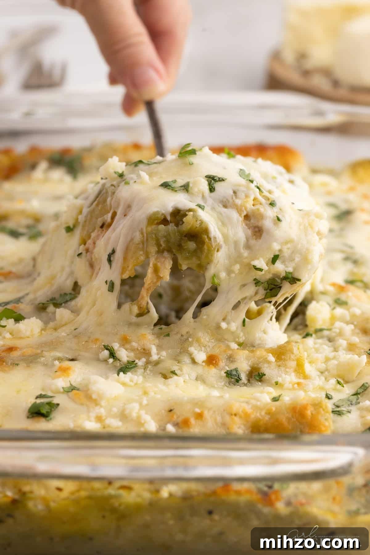A spoonful of Green Chicken Enchiladas being lifted from a 9x13.