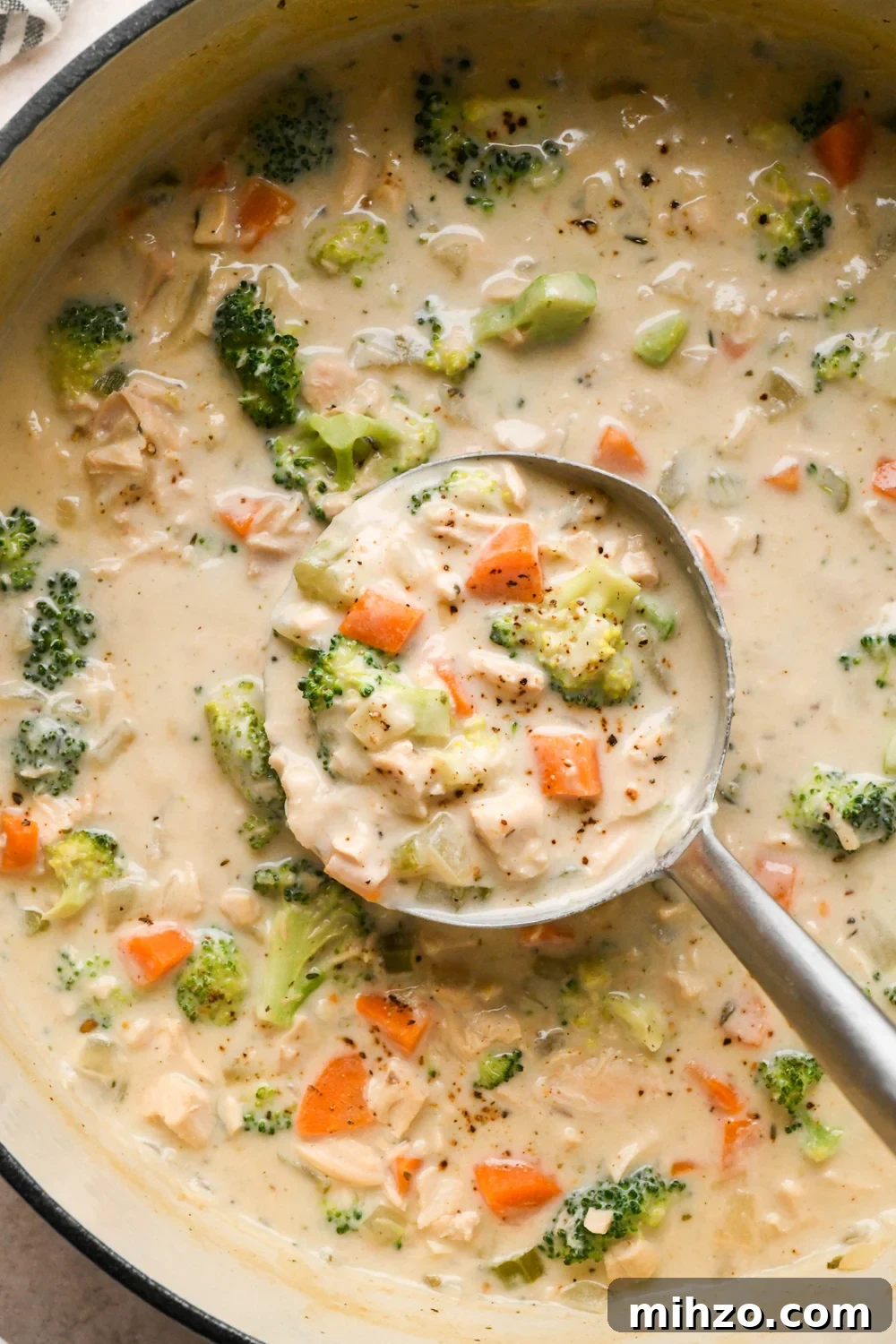 Delicious Dairy-Free Chicken and Broccoli Soup Recipe 18 A large white ceramic coated soup pot of creamy dairy free chicken and broccoli soup, with lots of broccoli florets. A ladle is dipping into the soup to lift out a portion for serving.