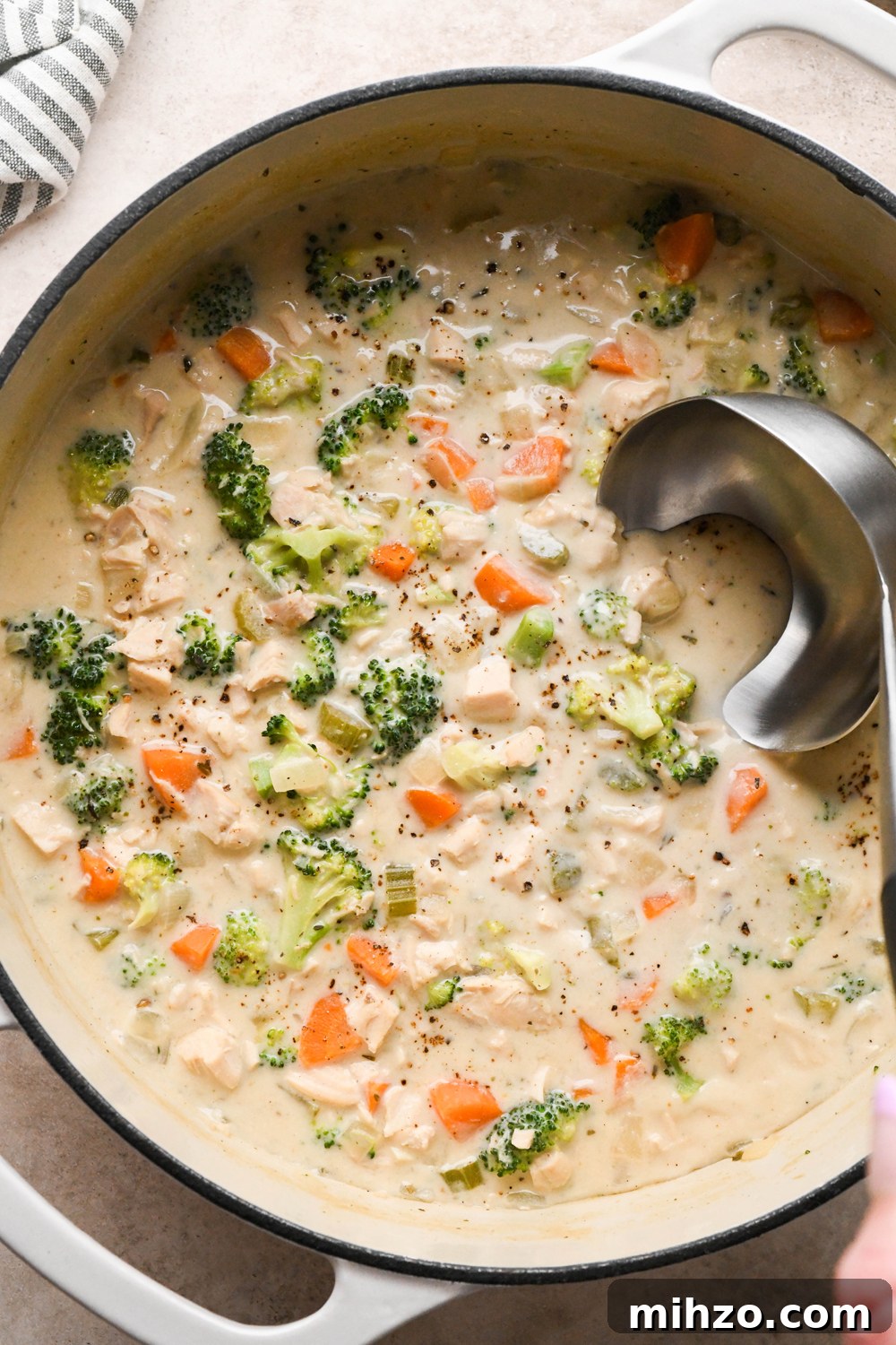 Delicious Dairy-Free Chicken and Broccoli Soup Recipe 3 A large white ceramic coated soup pot of creamy dairy free chicken and broccoli soup, with lots of broccoli florets. A ladle is dipping into the soup to lift out a portion for serving.