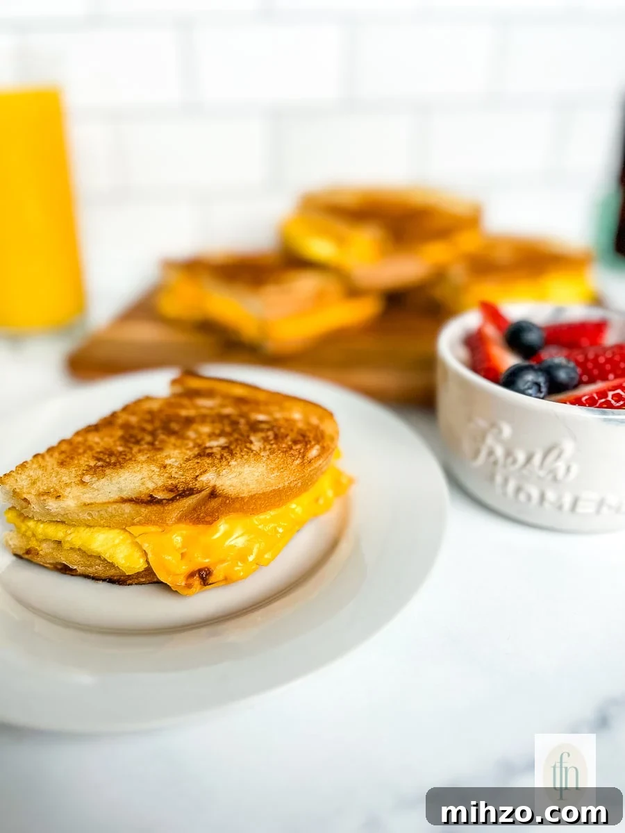 Sourdough Breakfast Sandwich Ideas for Quick Morning Meals 10 Grilled scrambled egg sandwich on a plate next to a bowl with fresh blueberries and strawberries.