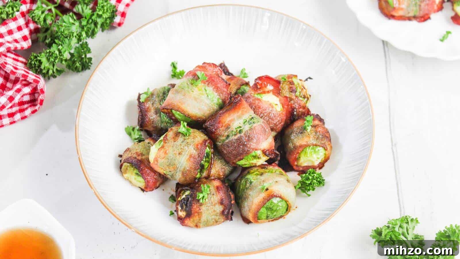 24 Brussels Sprouts Recipes That Even Non-Veggies Will Love 5 A white plate with bacon-wrapped Brussels sprouts garnished with parsley, placed on a white surface with a red checkered cloth and parsley nearby.