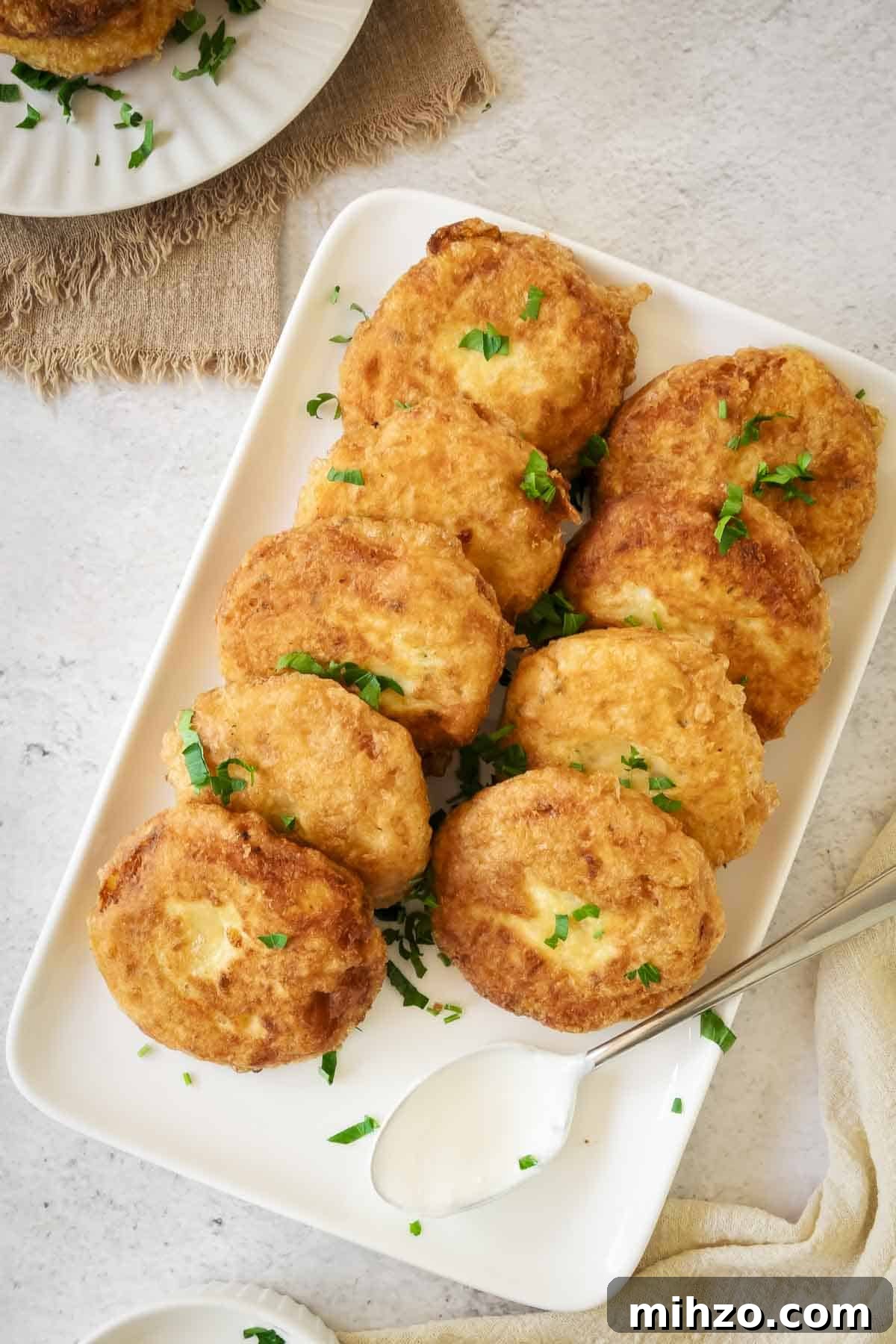 Crispy Potato Fritters Recipe — Golden Pan-Fried Latkes 2 Overhead shot of potato fritters on a white rectangle plate garnished with fresh parsley.
