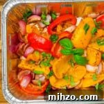 Smoked bell peppers and red onions in a disposable foil pan, seasoned and garnished with fresh chopped basil and whole basil leaves, ready to serve.