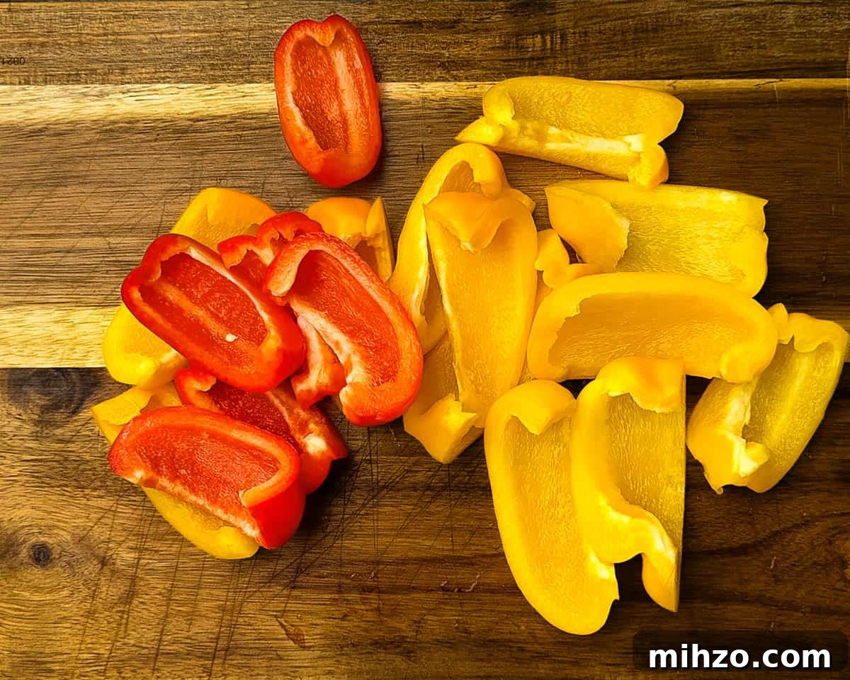 Sliced red and yellow bell peppers on a wooden cutting board, prepped and ready to be seasoned for smoking.