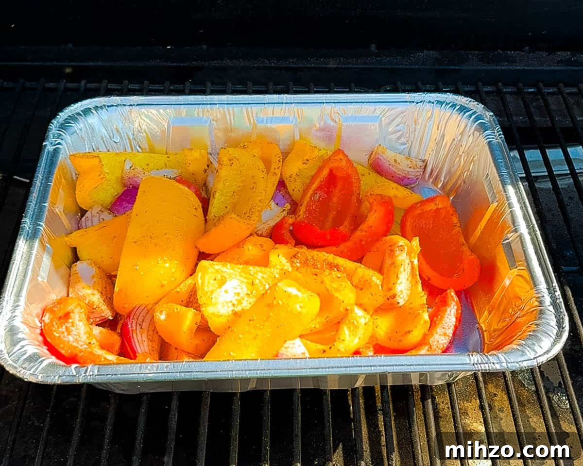 Foil pan filled with seasoned red onions and bell peppers placed on a pellet grill inside the smoker.