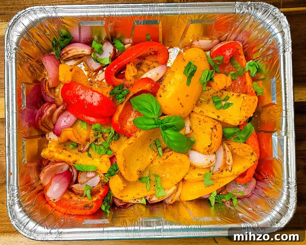 Smoked red onions and bell peppers with light char marks inside a foil pan, just pulled off the smoker.
