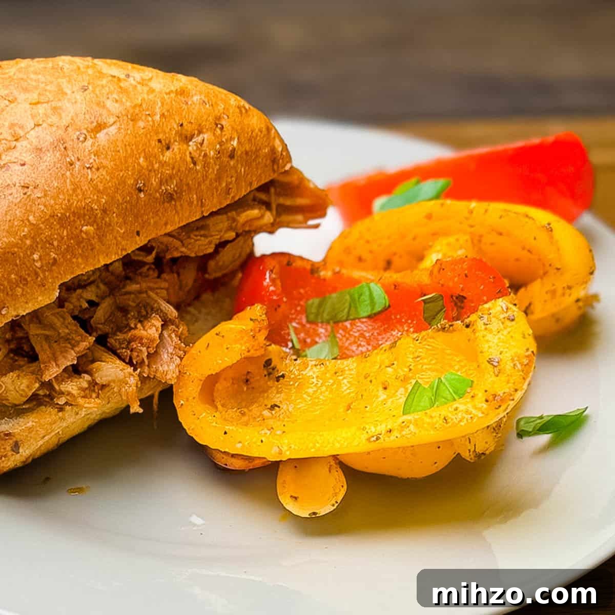 Smoked bell peppers and onions served on a plate next to a sandwich on a seeded whole wheat bun.