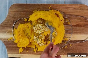 Cooked pie pumpkin on cutting board scooping out seeds.