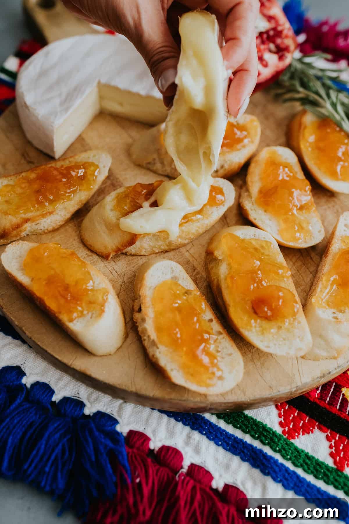 hand holding the rind of brie and drizzling out the melty interior to top the apricot preserves.