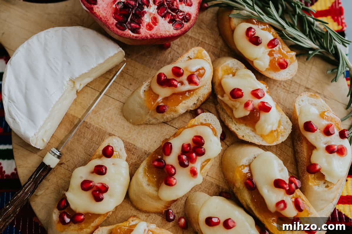 closeup shot of festive brie bruschetta crostini on a cutting board and topped with pomegranate arils for serving as an appetizer.