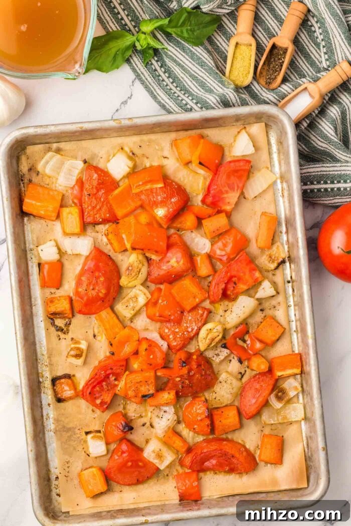 Roasted tomato, bell pepper, carrot and onion on a baking sheet lined with parchment paper.