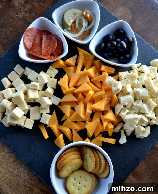 Meat and Cheese Board with three kinds of cheese on gray slate and using white bowls for olives and crackers.