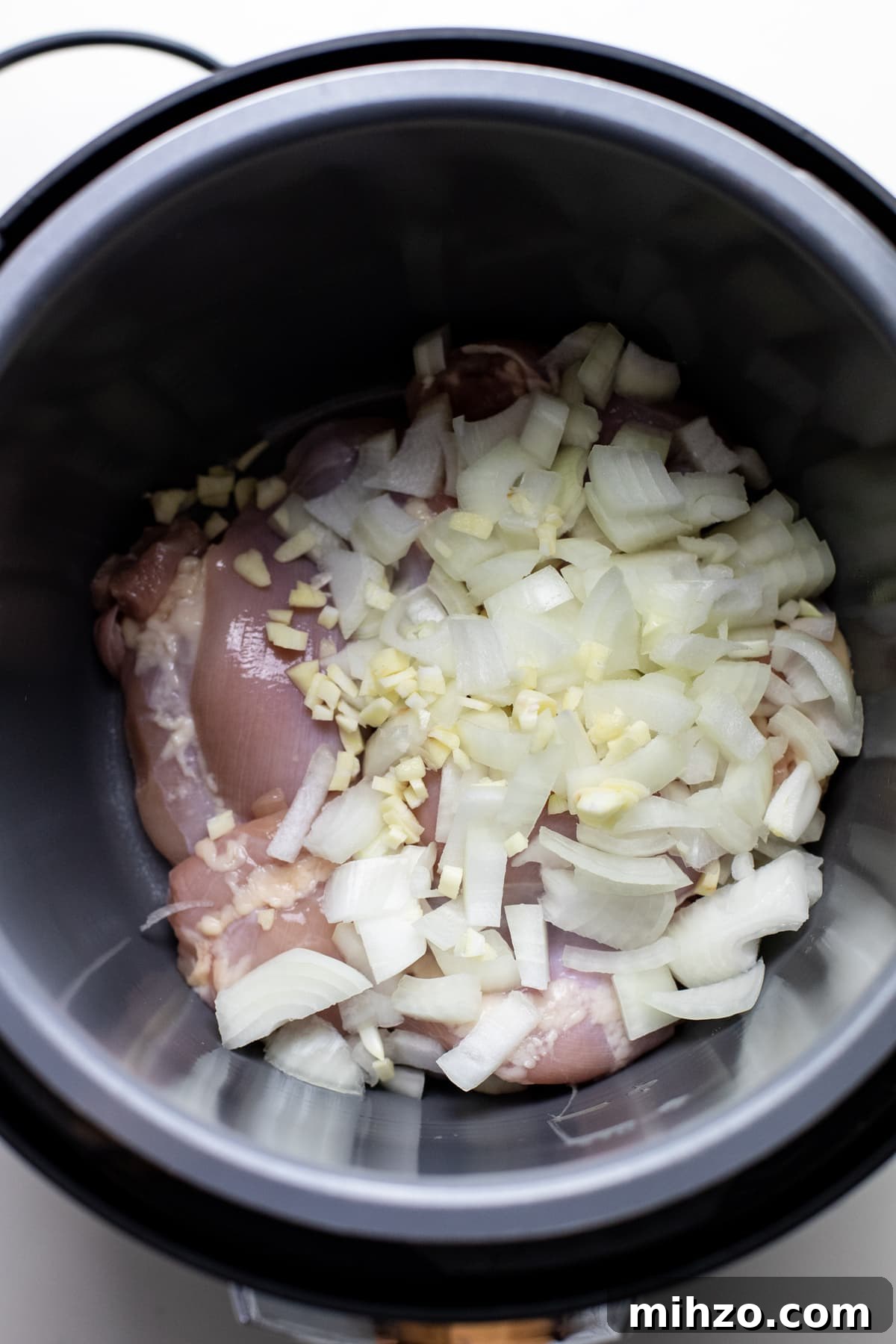 Slow-Cooker Chicken Chili Recipe for Cozy Weeknight Meals 3 A slow cooker pot with raw onions and raw chicken in it.