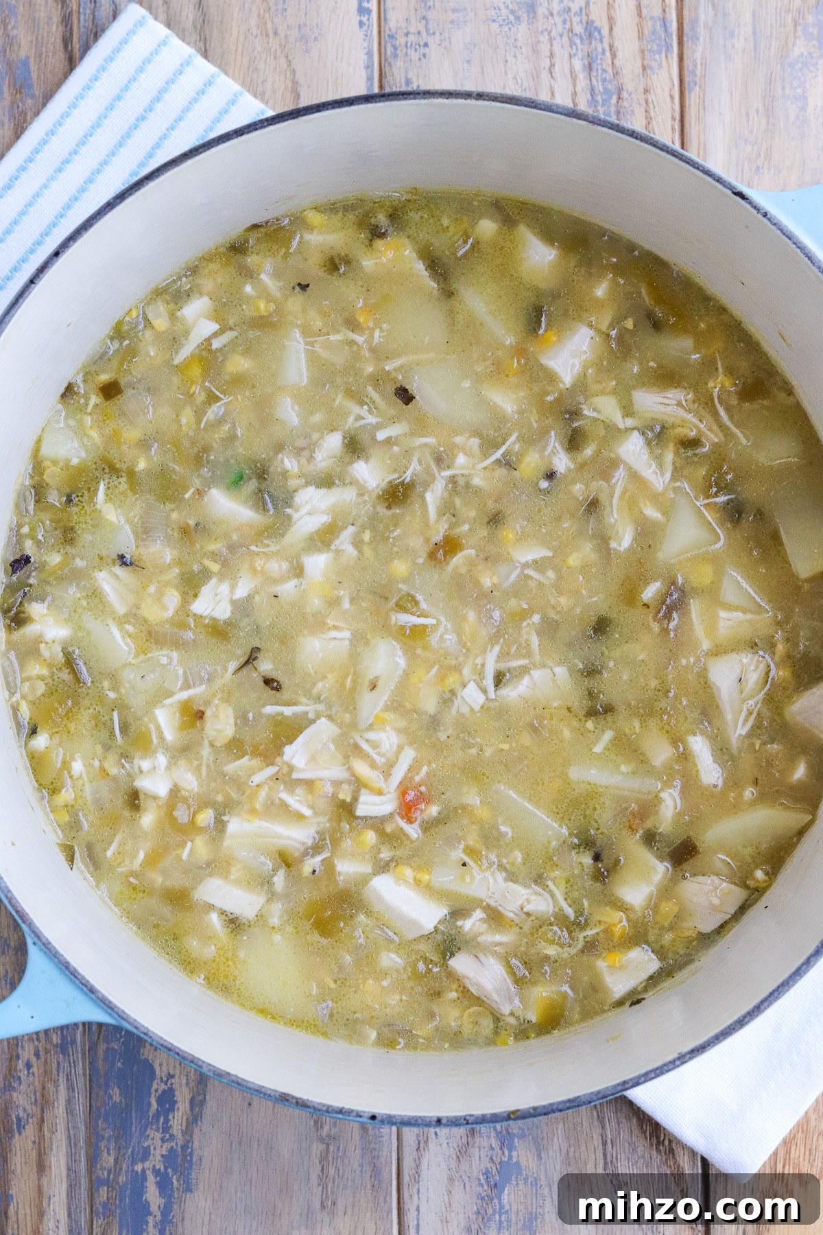dutch oven of cooked soup with visible potatoes and roasted hatch Green Chiles