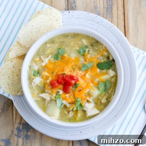 closeup of bowl of hatch green Chile chicken soup topped with cheese and tomato