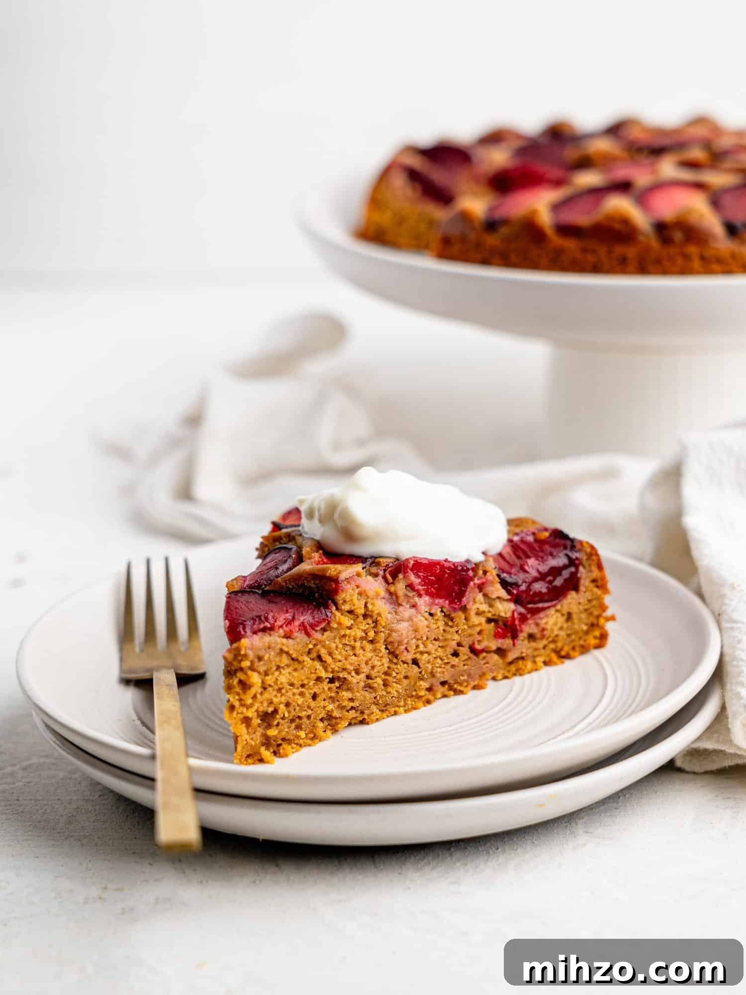 A slice of yogurt plum cake served with yogurt on a white plate.