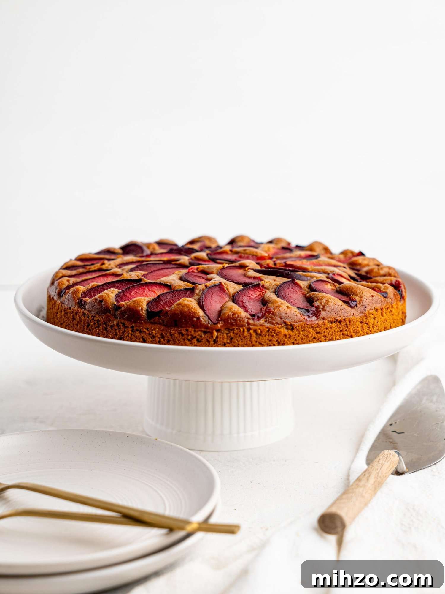 Yogurt plum cake on a white cake stand.