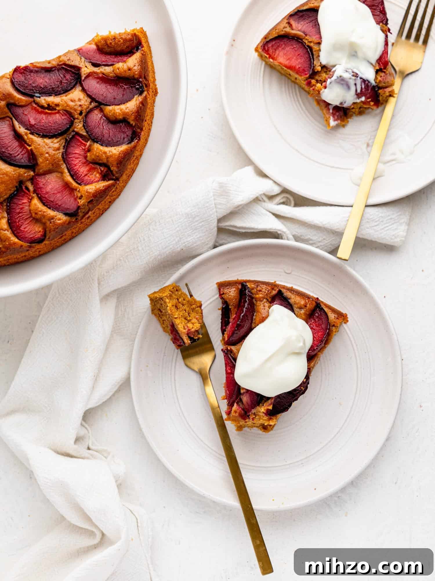 Bird's eye view of cake with plums served with yogurt on a white plate.