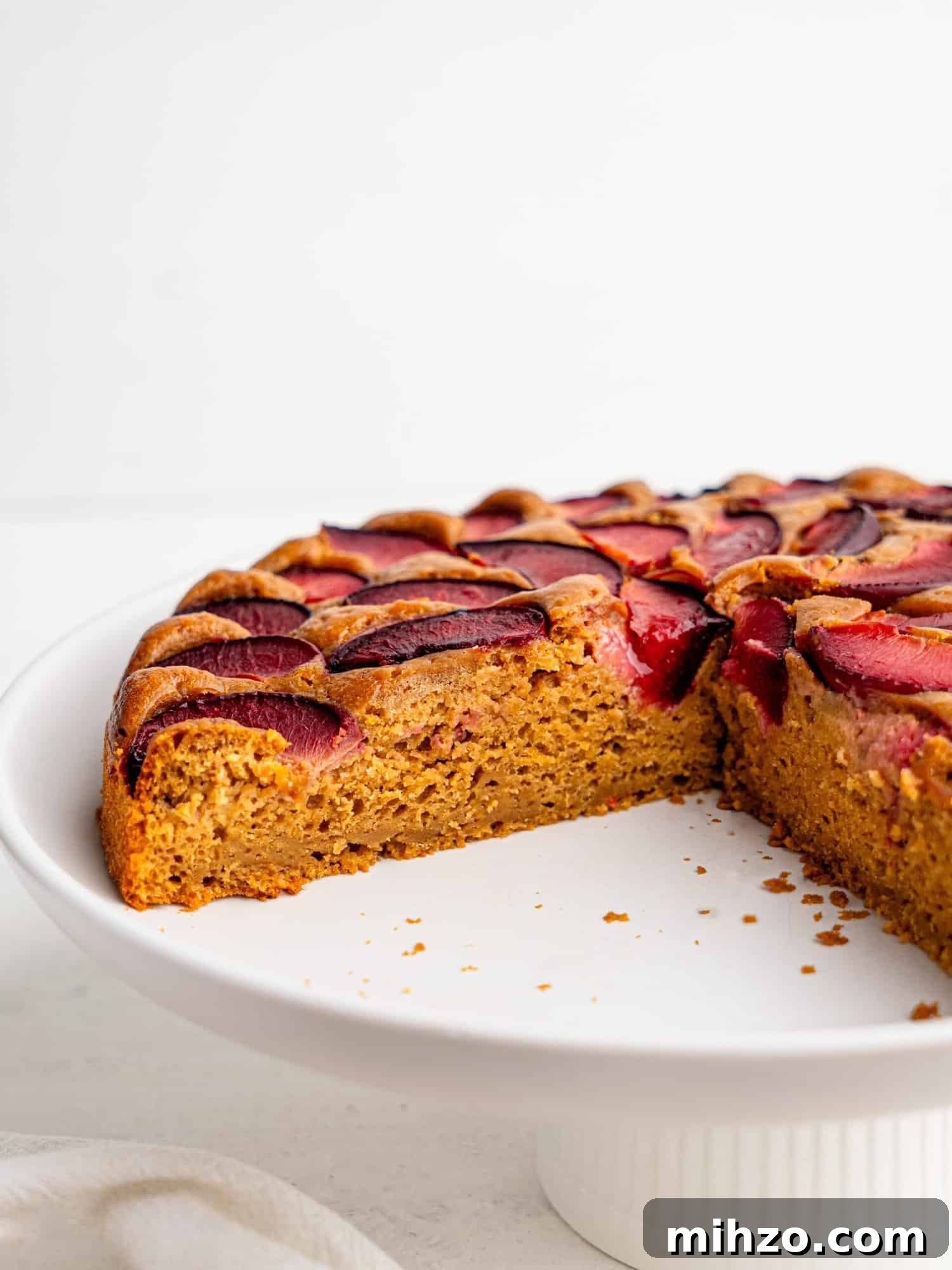Yogurt cake with plums on a white cake stand.